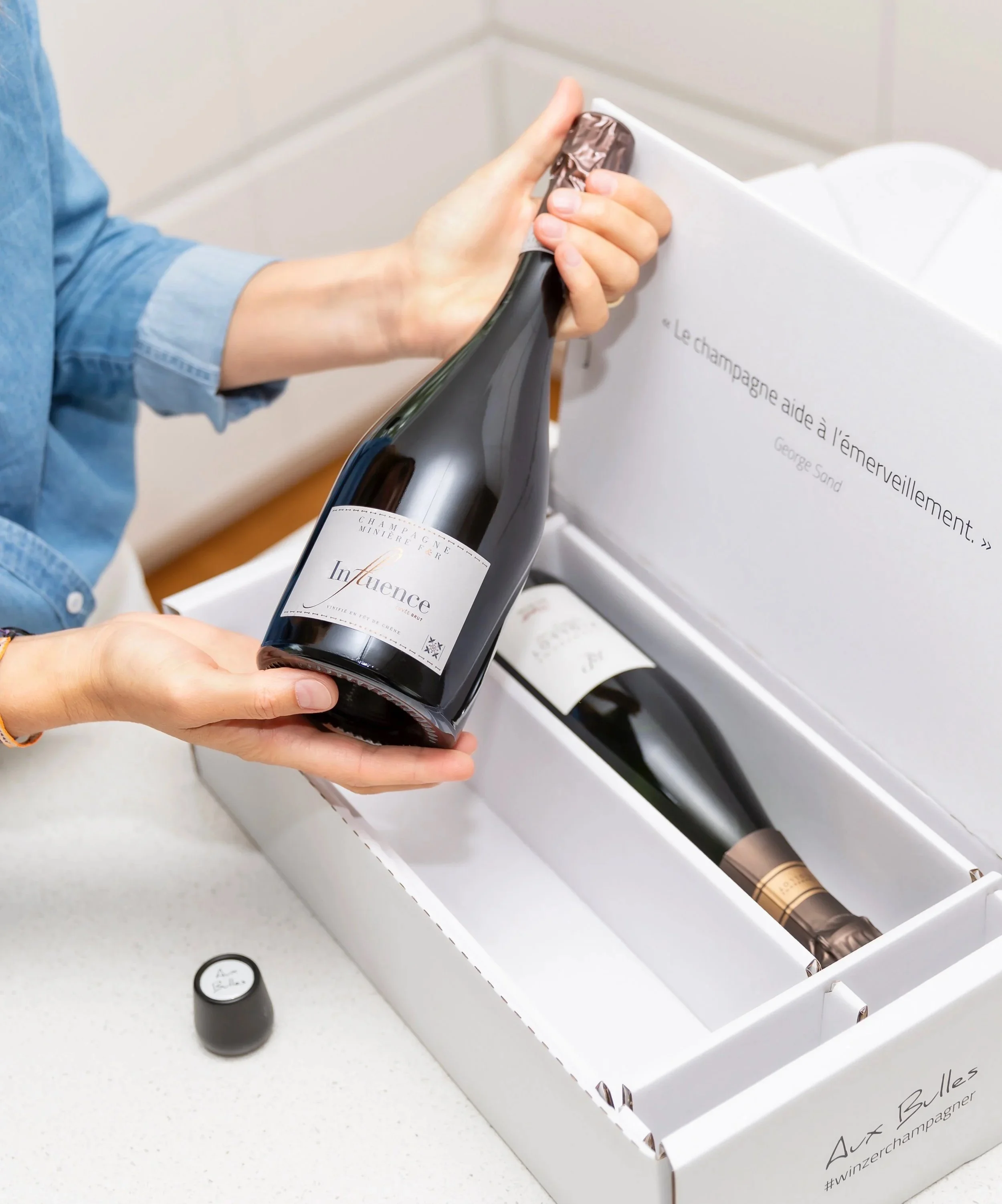 Aux Bulles Champagnerabobox mit zwei Flaschen Champagner. Eine Flasche wird gerade herausgenommen und dem Betrachter präsentiert