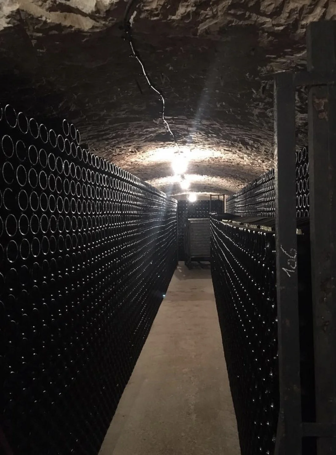 Win Keller in der Champagne. Rechts und links sieht man Flaschen aufgestapelt. Die gewölbte Decke ist durch einfache Glühbirnen beleuchtet