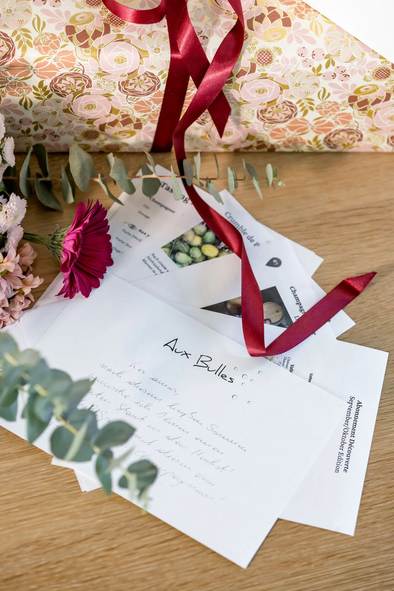 Champagnerabo als Geschenk von Aux Bulles mit liebevoll verpacktem Präsent, persönlicher Grußkarte, Blumen und rotem Geschenkband