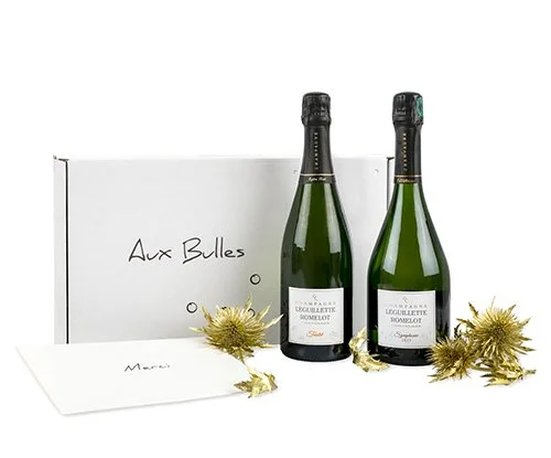 Zwei Flaschen Champagner vor einer Aux Bulles Champagnerabo Box davor ein Kuvert mit dem Text Merci und vergoldeten Disteln