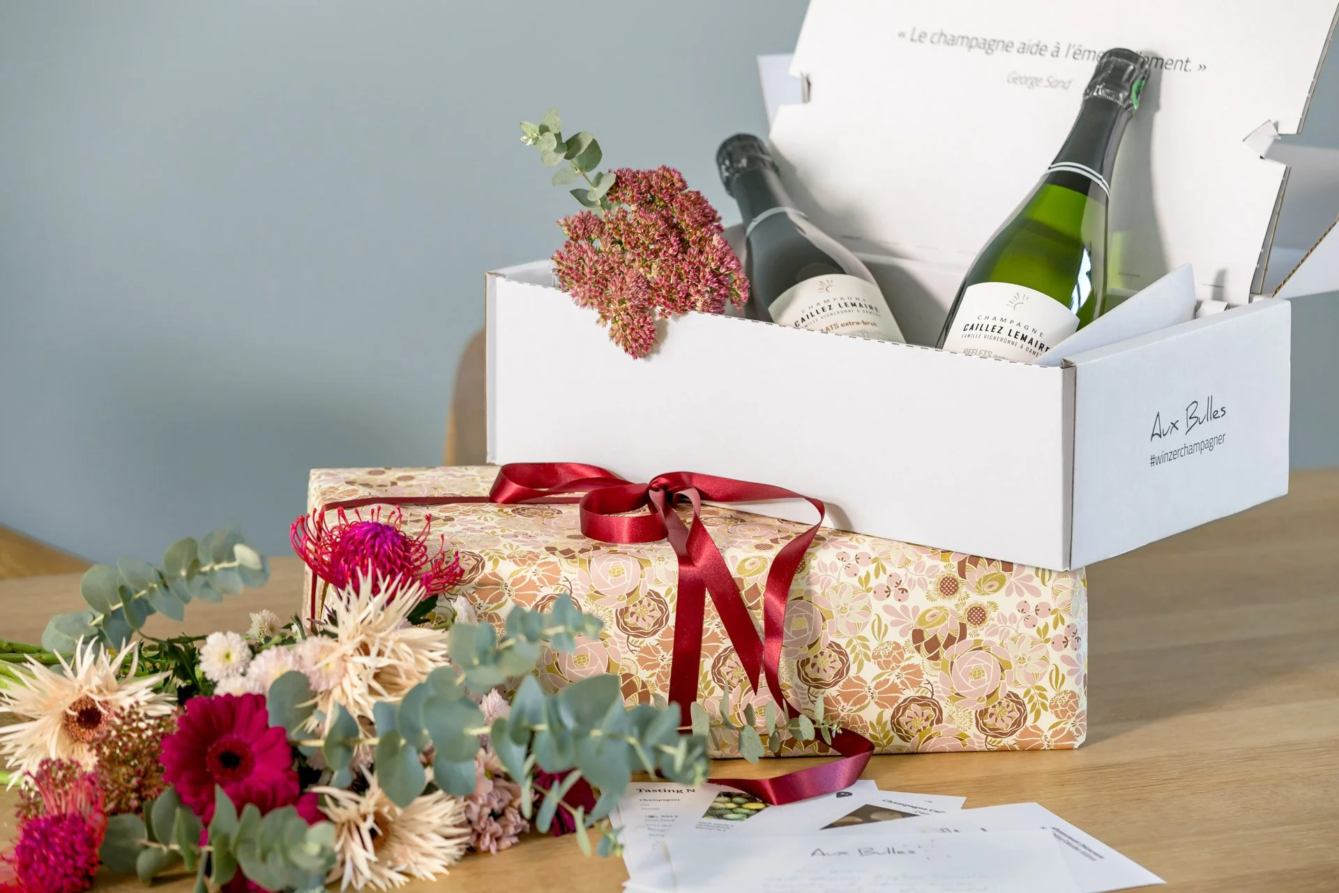 „Liebevoll verpackte Champagner-Geschenke von Aux Bulles mit ausgewählten Winzerchampagnern, Blumen und Geschenkband.“