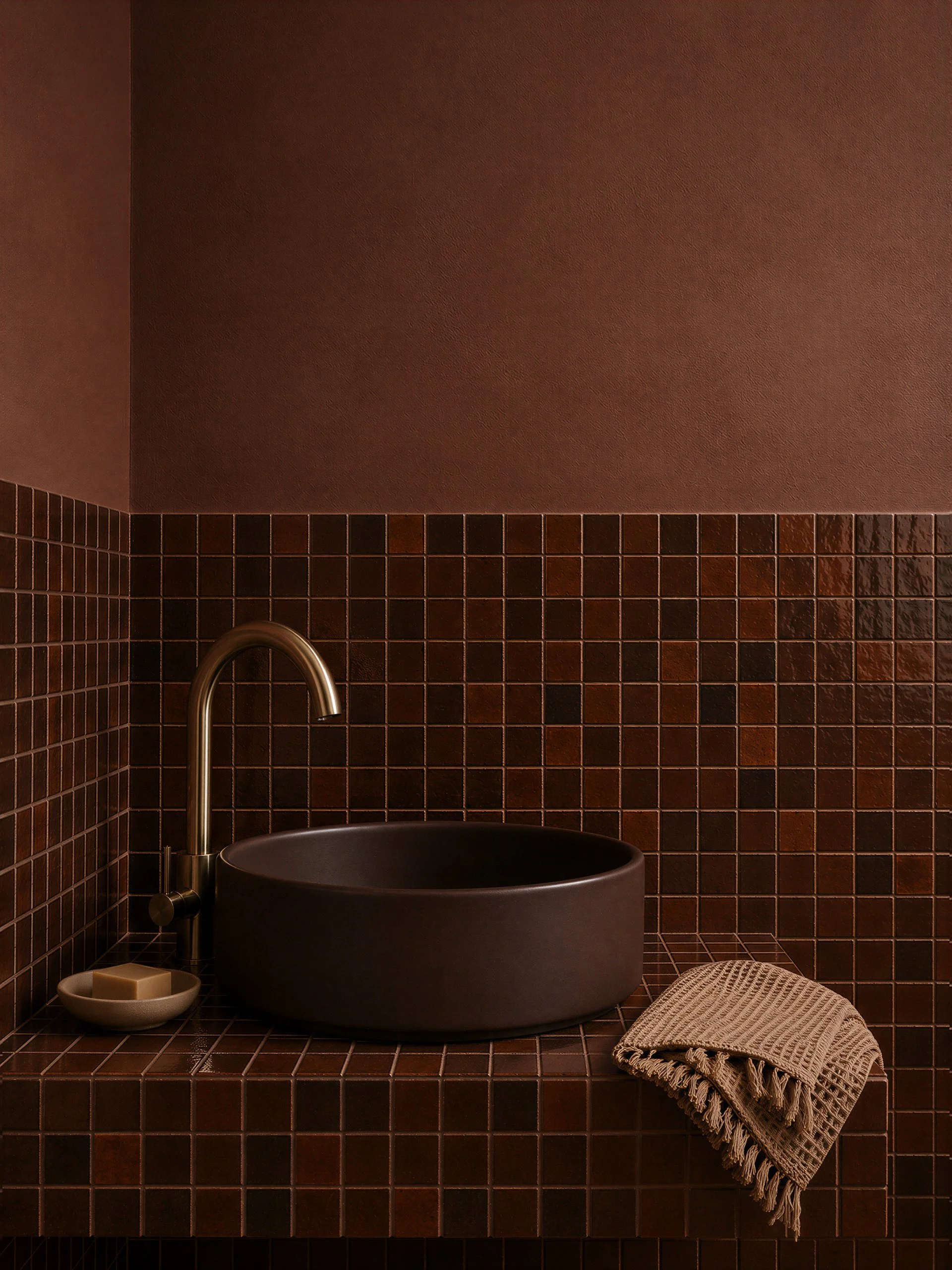 Dark brown concrete vessel sink in a warm tiled bathroom with bronze faucet, tonal walls, and textured materials.
