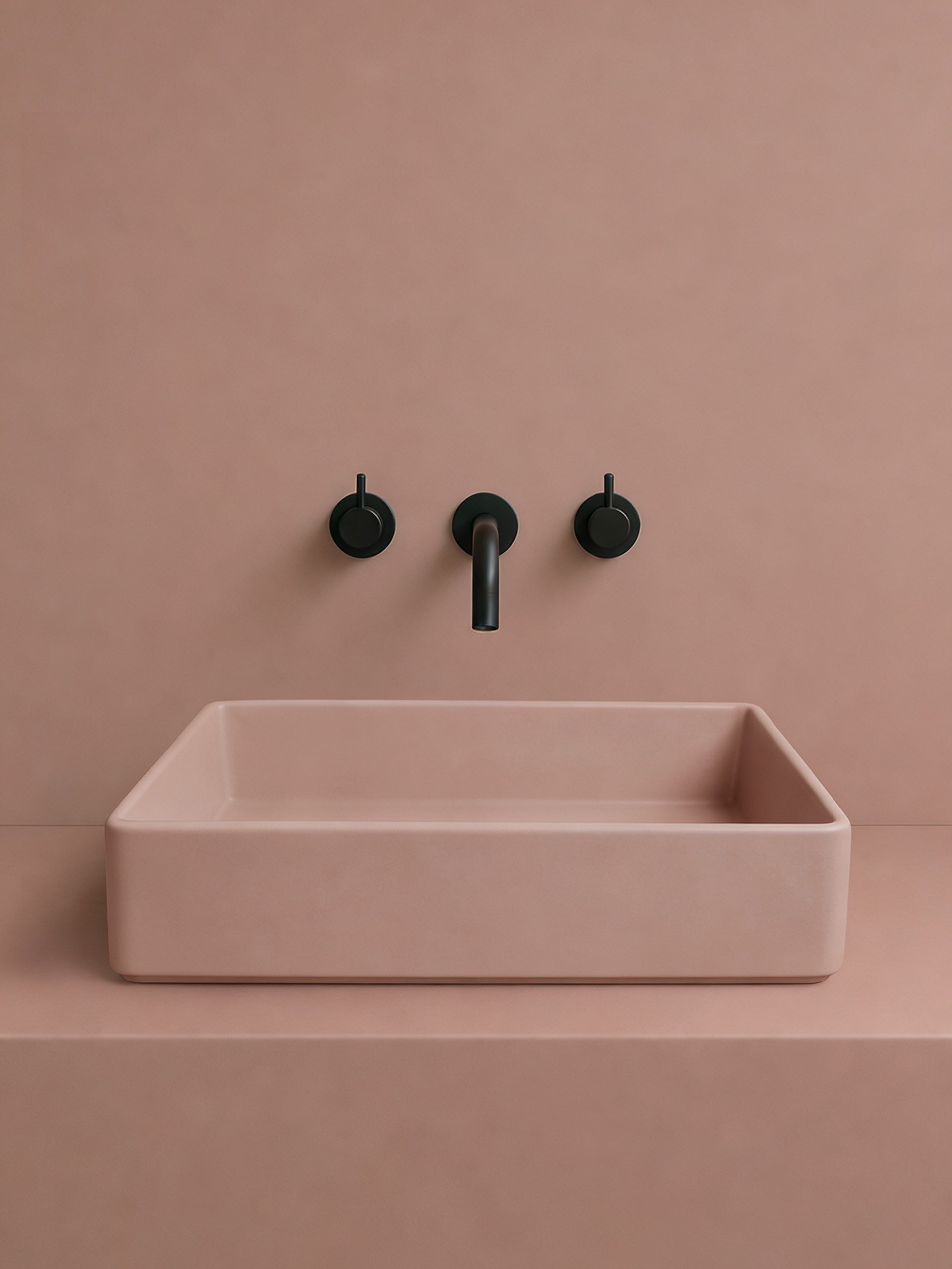 Rectangular blush pink concrete bathroom sink with softened edges and matte black wall-mounted faucet on a monochromatic pink backdrop.