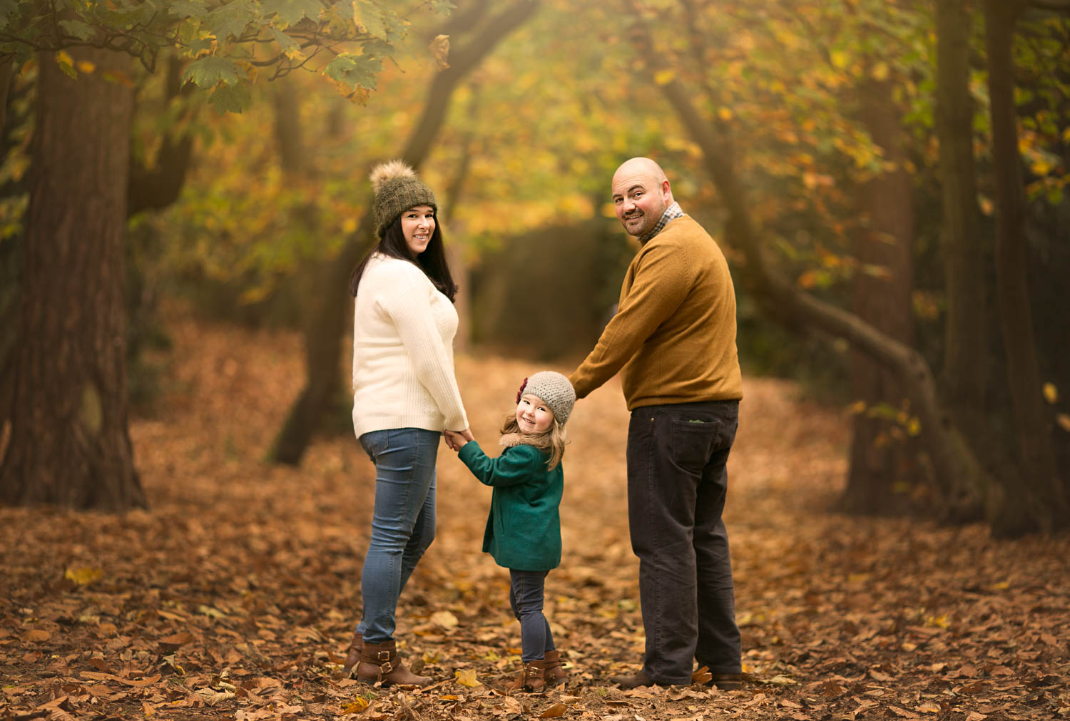  Mother, father and daughter looking over their shoulders in woodland duirng a family autumn photoshoot at Ampthill Park in Bedford. 