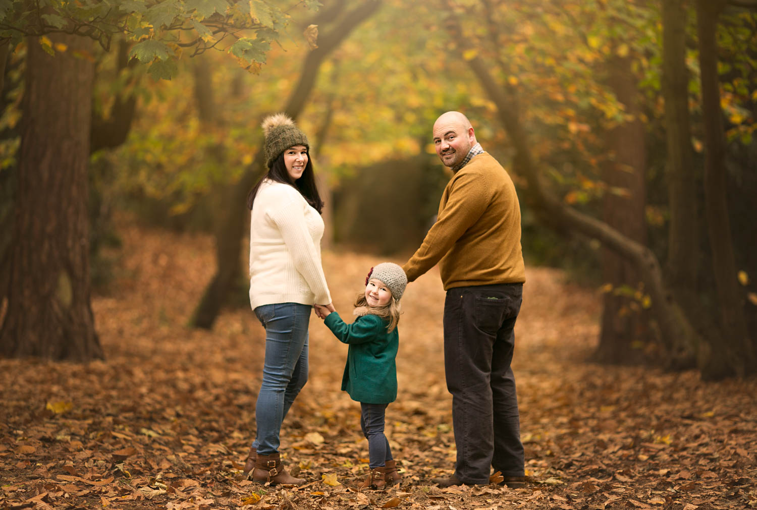 Mother, father and daughter looking over their shoulders in woodland duirng a family autumn photoshoot at Ampthill Park in Bedford.