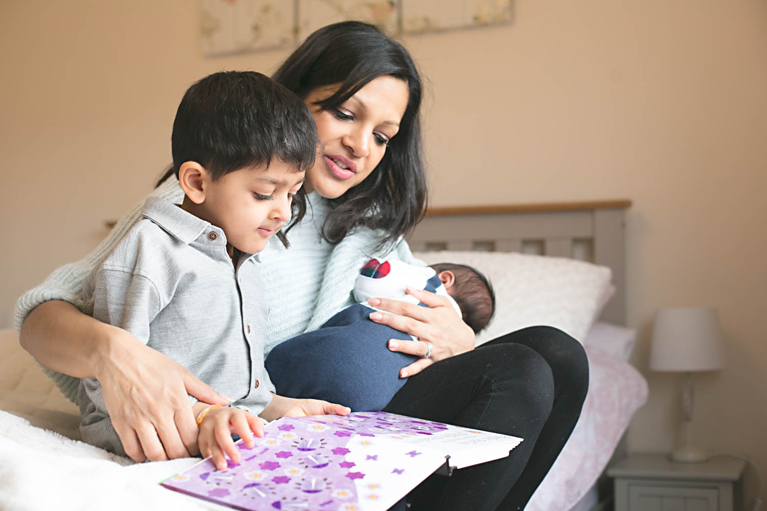  Mother reading to her son whilst hilding her newborn baby during a lifestyle shoot in Bedford. 