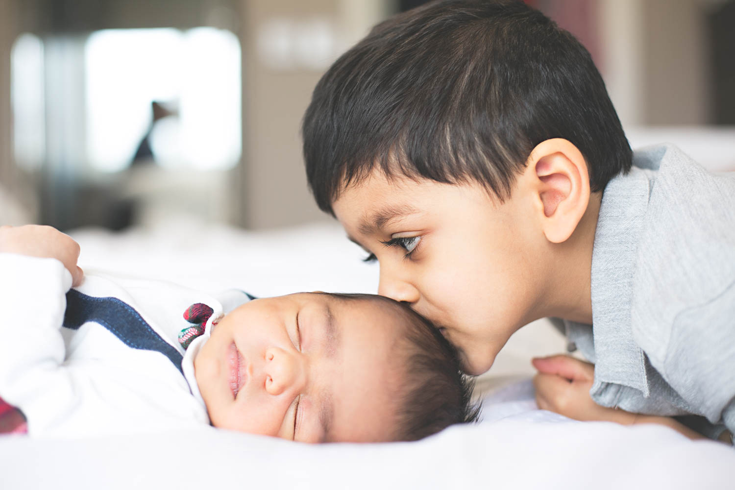  Brother kissing baby brother's head during a Newborn lifestyle photoshoot in Bedford. 