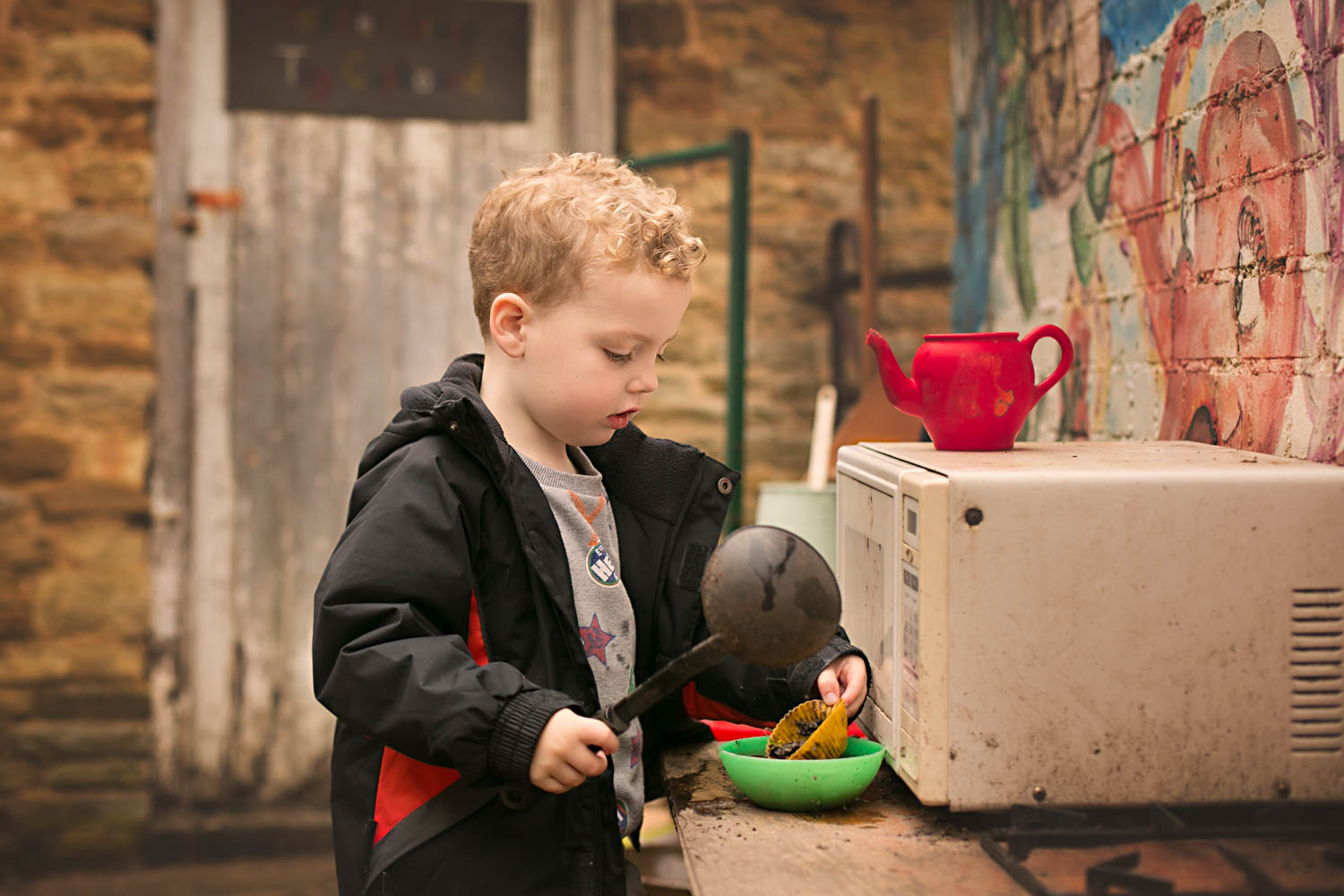 boy playing in outdoor kitchin during a preschool photoshoot in Turvey, Bedfordshire.