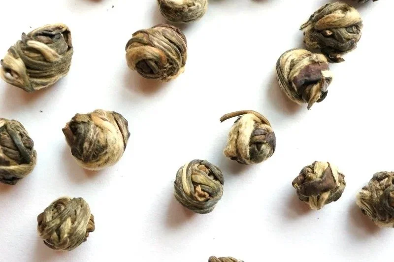 Loose Jasmine Dragon Pearls, small hand-rolled balls of green tea leaves, on a white surface