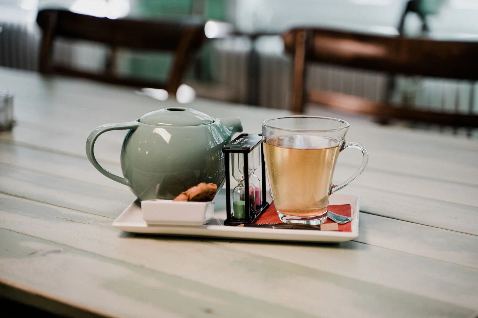 A green ceramic teapot next to a glass cup of tea on a wooden table.