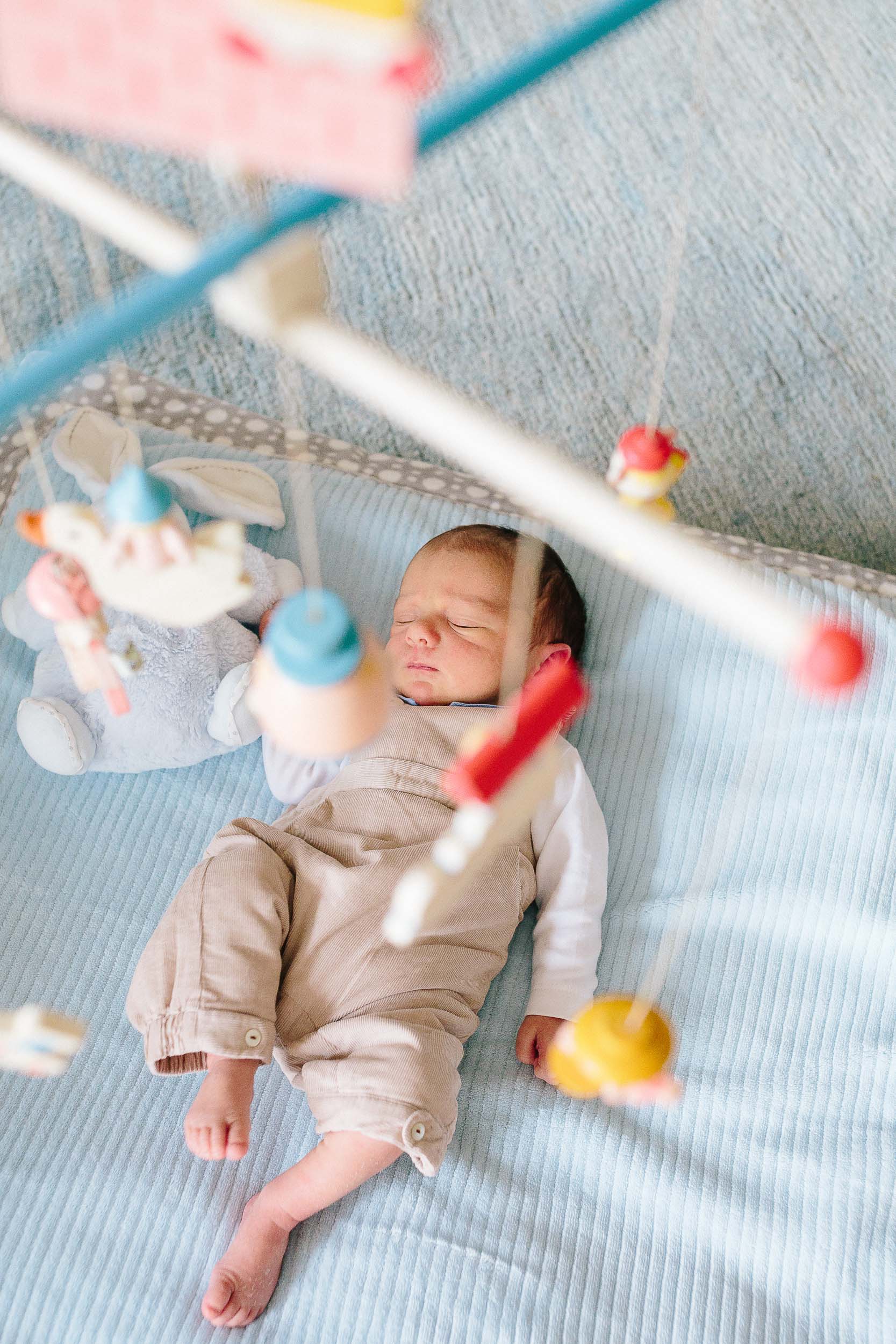 A newborn baby boy lies on his mat with a mobile hanging above him.