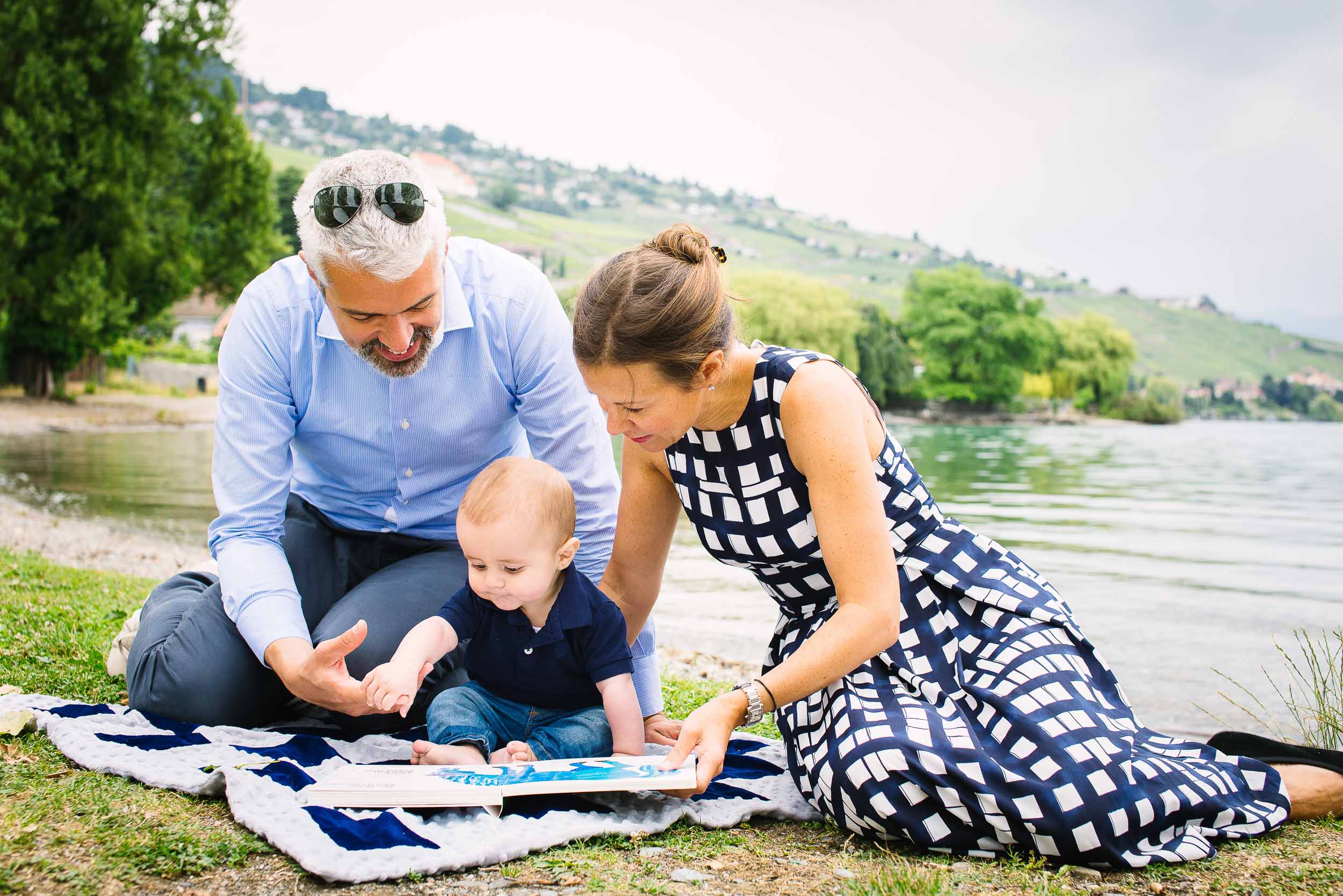Parents read to 6 month old baby boy on shore of Lake.