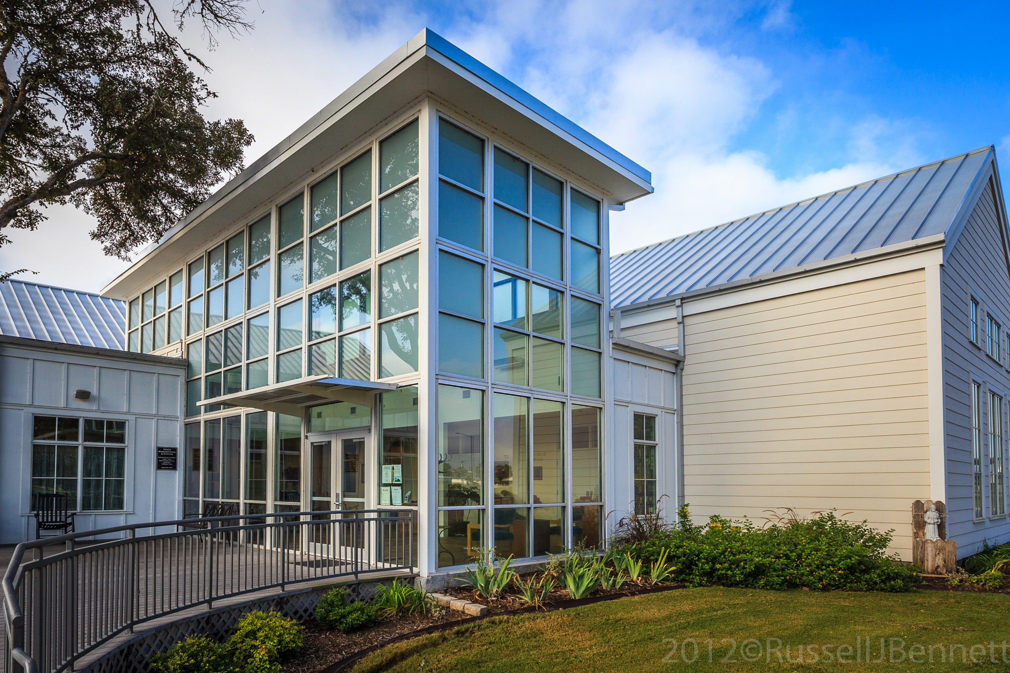 The Kolíbá Lobby invites visitors in to the TCHCC Main Center/Office/Library/Museum/Archives building which houses the offices, Hanslik Hall Dining & Meeting Room, the Willie and Mardi Kopečky Gift Shop, KJT Conference Room, the Bill and Betty Melnar Library, where genealogy and historical research can be accomplished, and the Nás Nový Domov ( Our New Home ) Museum, which displays the many artifacts and memorabilia that have been donated to TCHCC and tells the story of the early Czech-Texans. This Main Center building, designed by architect Roger Kolář, was completed in October of 2009. The building has a contemporary glass entrance representing the beacon of light that attracted the settlers to Texas and also brings to mind the 19th century farm houses, halls and buildings, but is not a duplication of them. At the entrance, paving stones, brick memorials and the Immigrants’ Wall honors family and friends. A memorial brick walk leads to the three flags which our Czech ancestors treasured: the United States Flag, the Flag of the Czech Republic, and the State of Texas Flag.