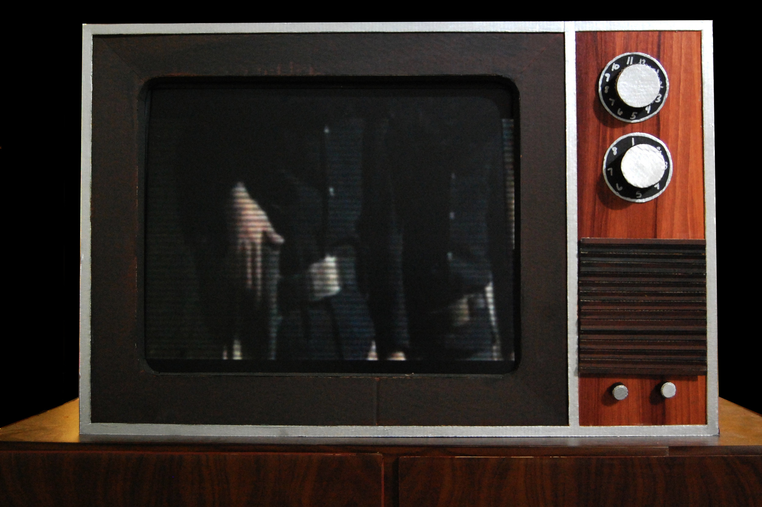 Betty Kelly created American Trauma, a sound and video installation, to explore the indelible link between the American Identity and Gun Culture. The installation, a 1960’s family room built almost entirely out of cardboard, is comprised of four