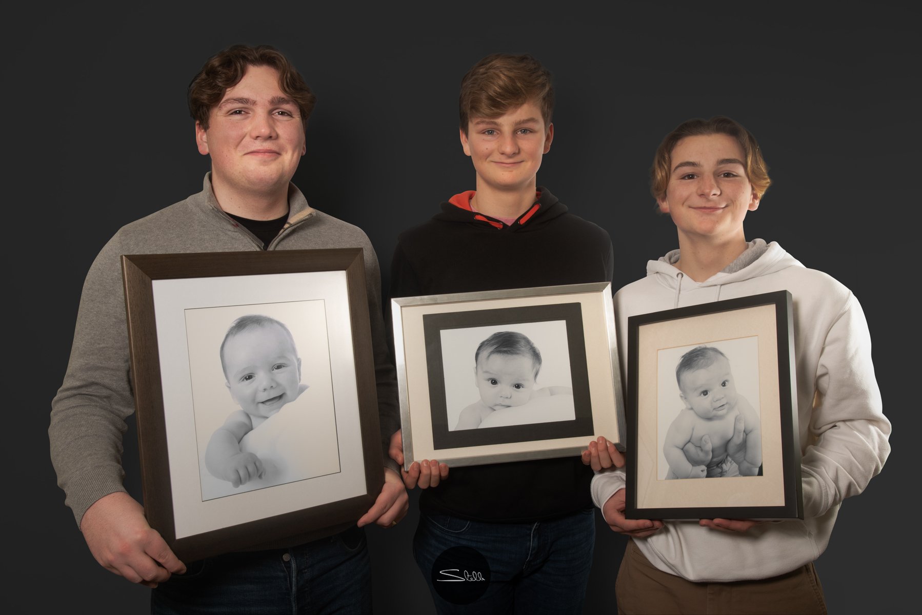  Brothers holding photographs of them each at 3 months old. 