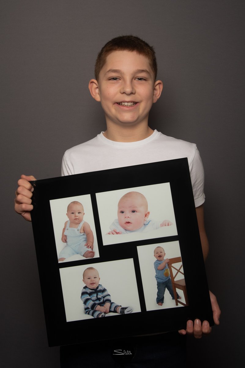  This young man holding framed photographs taken of him at 3, 6, 9 and 12 months… 