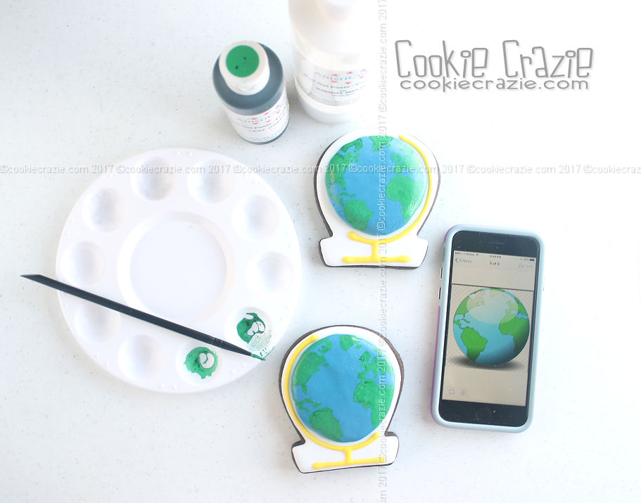  After the blue globe has dried for a few hours, use a map of the world to paint a rough outline of some of the continents with green glaze.&nbsp; 