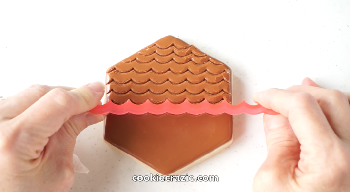 After the hexagon has dried for approximately 2 hours, use the scalloped edger from SweetSugarBelle's Shapeshifter's set to create rows of feather marks down the cookie as seen in the photo and video.