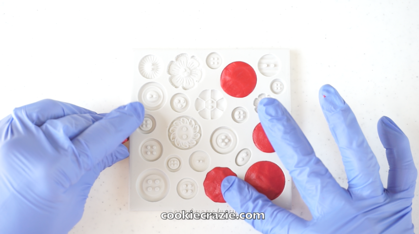  Completely fill a silicone button mold with red edible clay. (Mold shown found  HERE .) Place the filled mold in the freezer for 1 hour or more.&nbsp; 