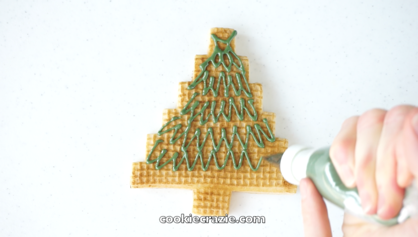  For the first design, cover the tree portion of the cookie with green glaze using random zig zag lines. (see photo and video for more visual details) 