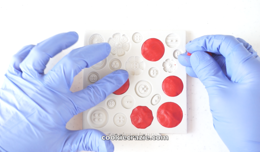 Completely fill a silicone button mold with red edible clay. (Recipe for clay found HERE & Mold used found HERE .) Place the filled mold in the freezer for at least one hour.