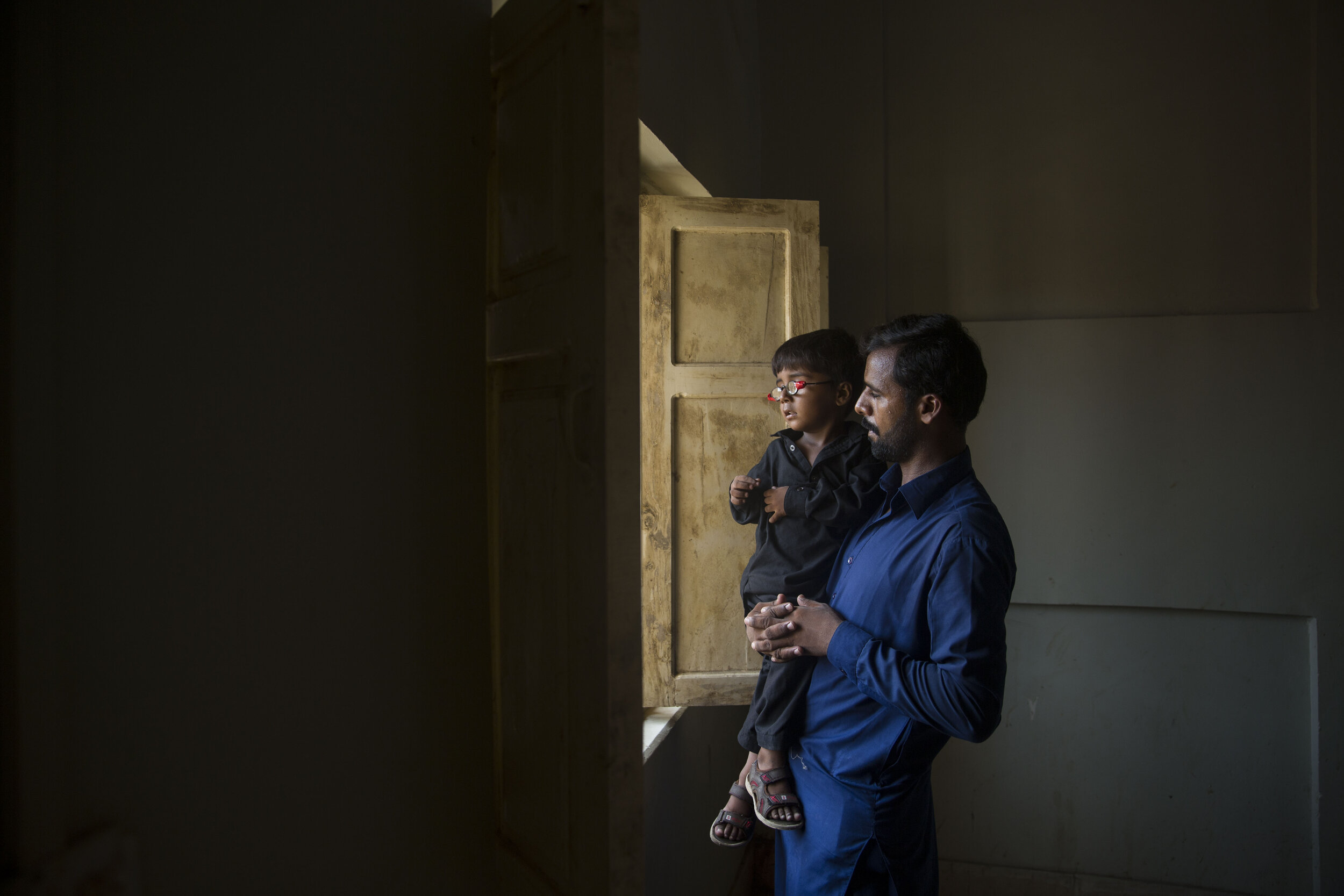  4-year-old Habibullah who has been diagnosed with HIV stands with his father and looks out the window at Sheikh Zaid Hospital on July 26, 2019 in Larkana, Sind, Pakistan. 