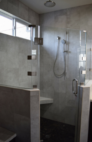 Corner shower with stone shower pan, a ceiling rain shower head, corner bench with built in shampoo storage, and wall hand held sprayer.