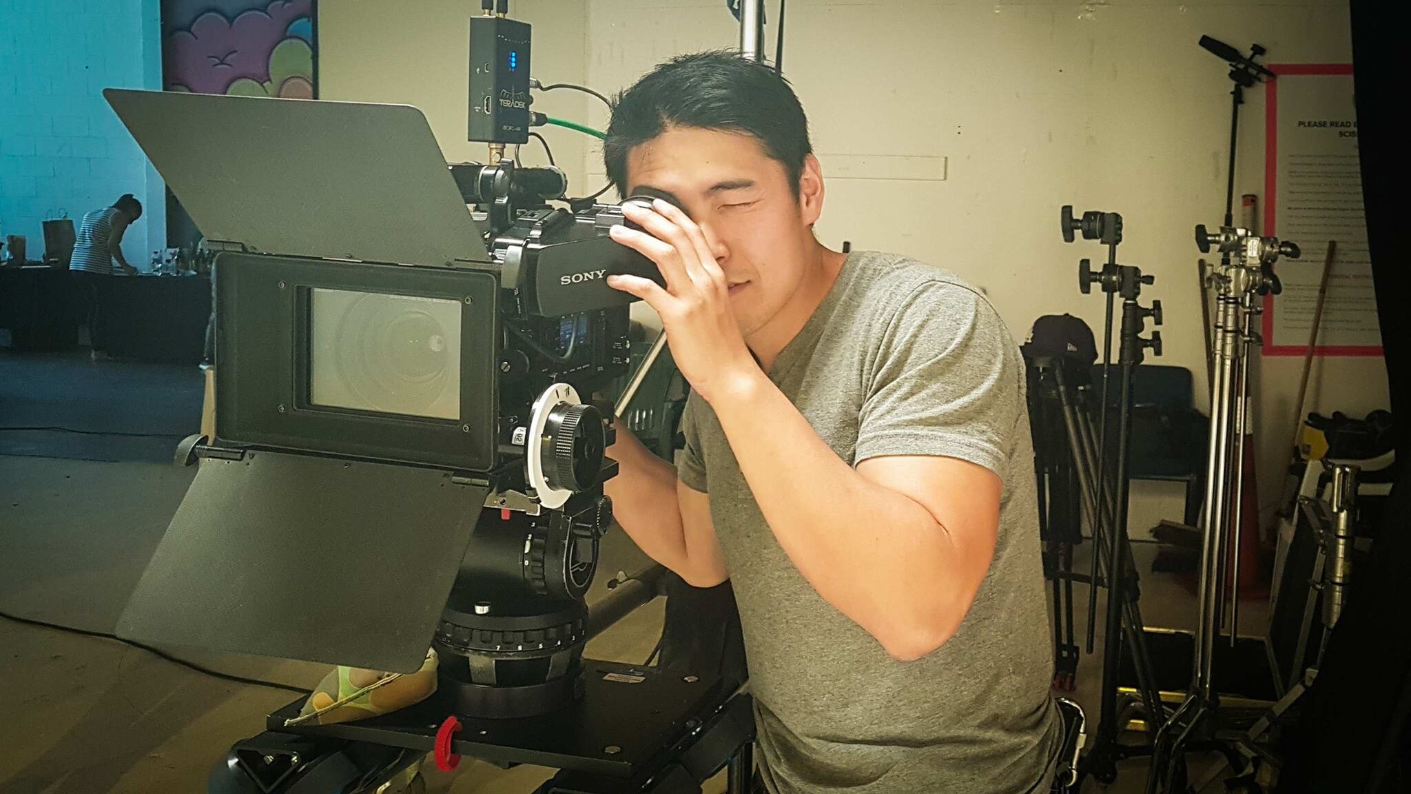 A man operating a professional film camera on a green screen set, with film equipment and crew members in the background.