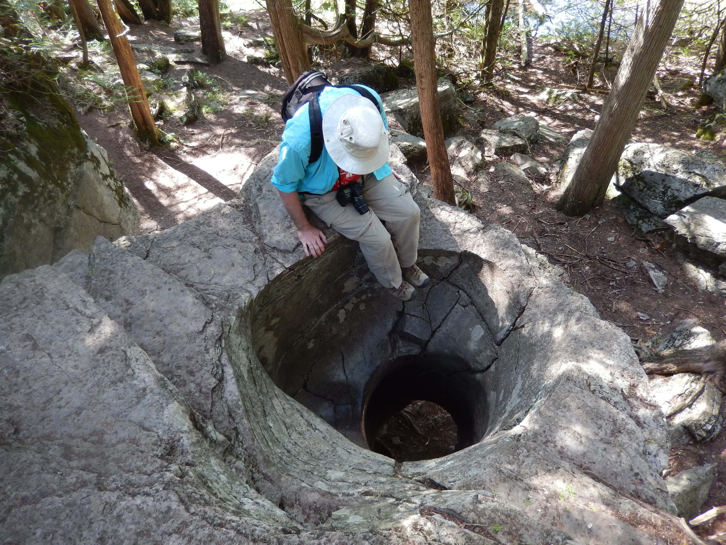 Andy Fyon sitting on the edge of a geological feature - a hole - called a pothole. The pothole was formed perhaps 10,000 years ago during, and at the end of, the last great ice age when rushing water carried pebbles that drilled into the rock. At that time, this rock surface was the floor of a rushing river fed by glacial meltwater. Location: Warsaw Caves Conservation Area. Photo by E. Ginn, 2016.