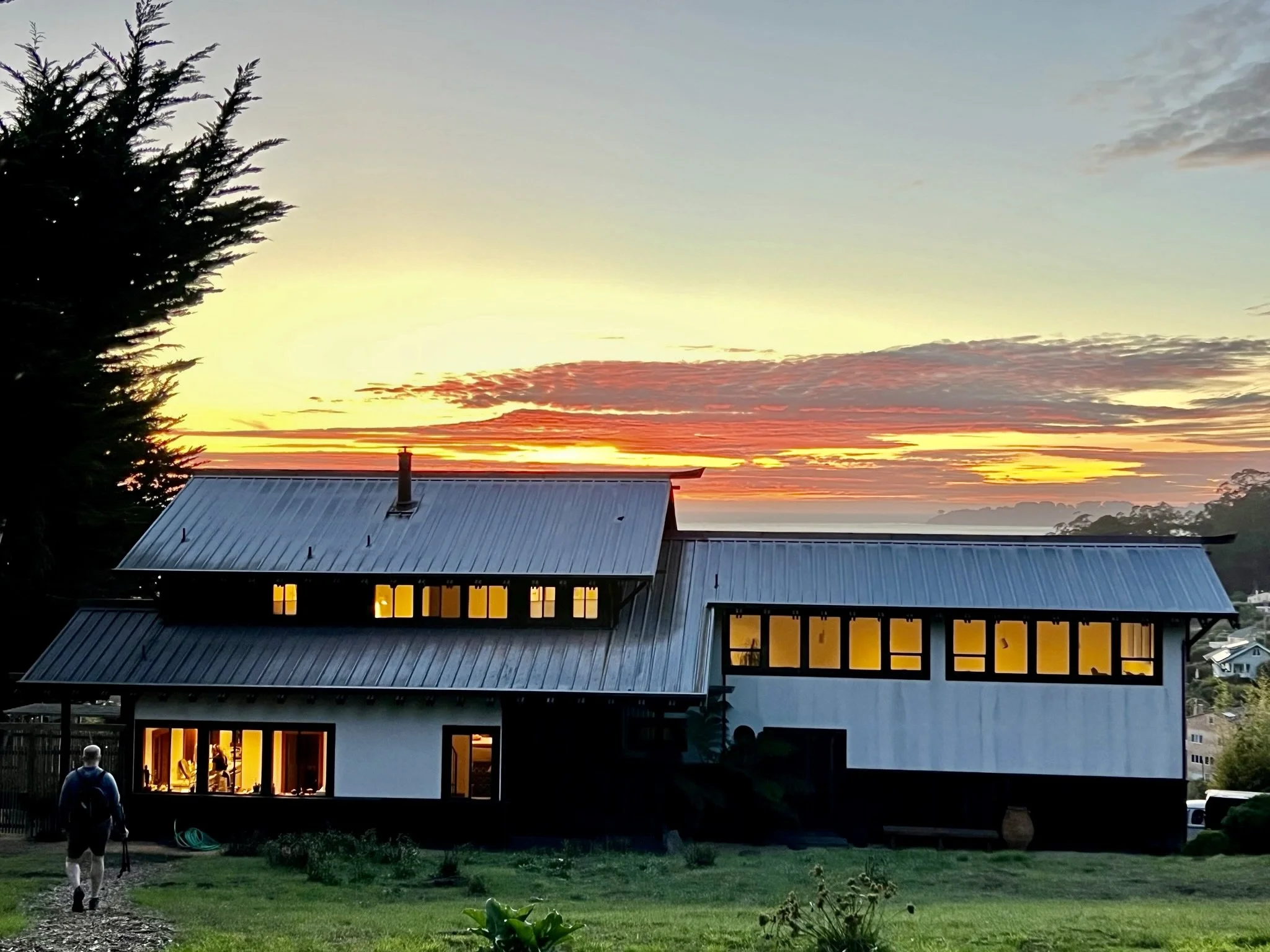Kenko Retreat, set against a sunset sky with orange, pink, and yellow hues. A person returning from a hike to a beautiful base. 