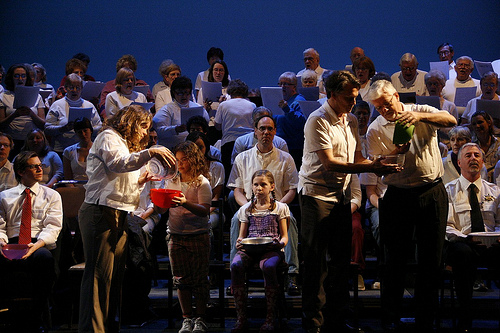 Picture of the choir singing and actors pouring water into each other’s bowl.