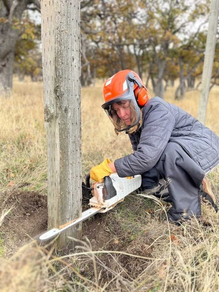person chainsawing a post in the ground