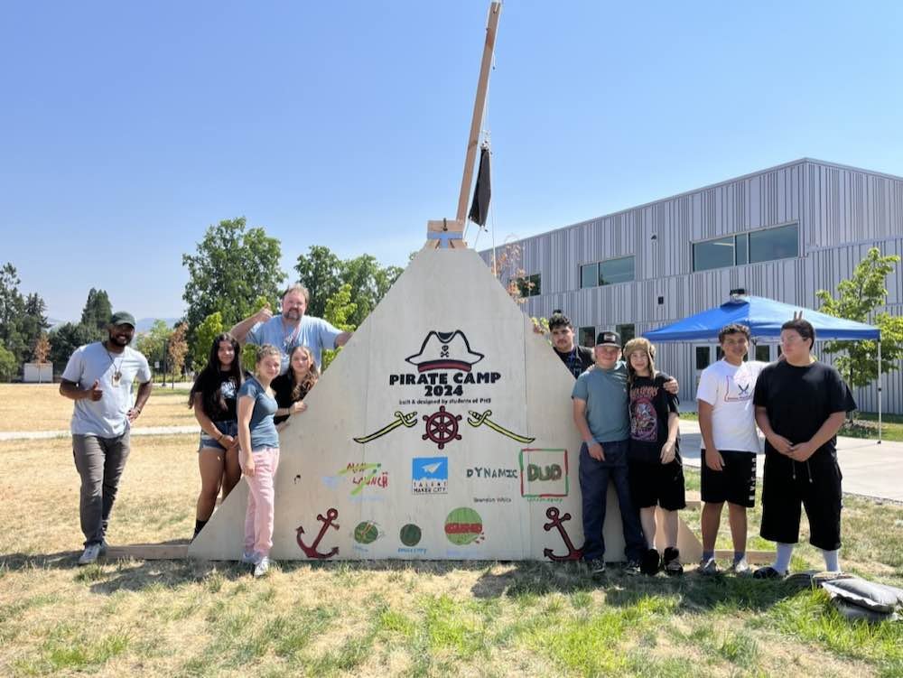 Students surrounding a handmade triangular wooden catapult