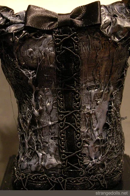 Her dress is made from a mixture of garbage bags, cheesecloth and rubber, rough and tough recycled materials - topped off with delicate details like her satin ribbon and velvety trim. She sits proudly on a wood base. 