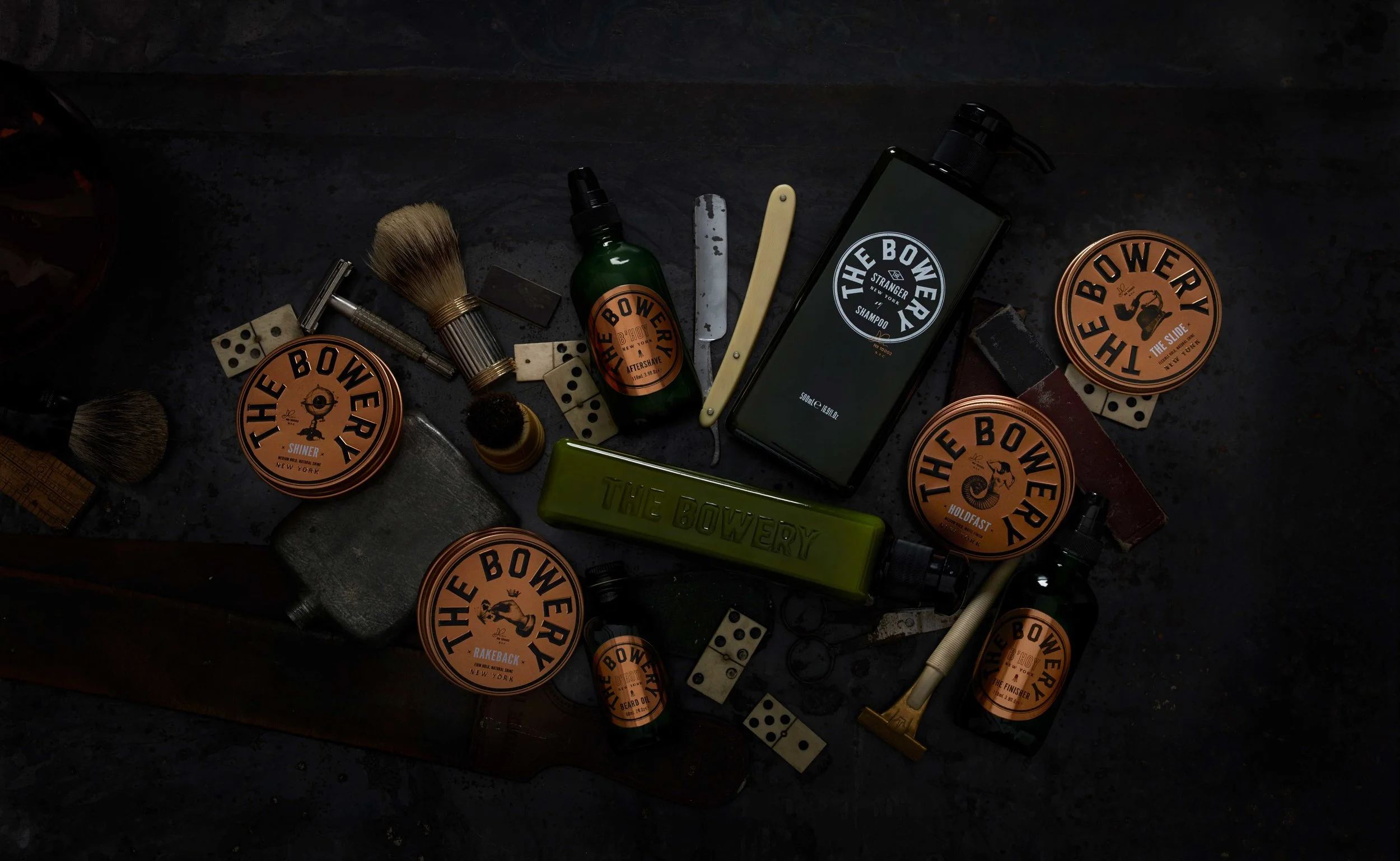 The first part of the process was to research the competitive set within New Zealand and from around the world. This allowed us to gain an insight into the market, but also ensured that our design solution would be unique. Concurrently we also dived into the overall influences and drivers for our target market. This was not specific to mens grooming products though, it was more lifestyle encompassing to cover fashion, music and other relevant social trends. Once this exploration was completed, it provided us a consumer snapshot to base the new brand on. Then came the fun part! Copious amounts of hours reading up about the history and culture of New York. There were various potential avenues that we identified going through this process, but the most interesting to us was a notorious area of the city called The Bowery. According to Theodore Roosevelt it was ‘one of the great highways of humanity. A highway of seething life, of varied interest, of fun, of work, of sordid and terrible tragedy’. Colourful characters with alternative lifestyles have long been stitched into the social fabric of The Bowery, creating a culture of attitude that really resonates with contemporary life. Our goal then was to weave these people and stories into a relevant way for the brand. This is where the stars really aligned. All of the legends that we featured for the individual products allowed us to create names that had abstract links to the product benefits. ‘Shiner’, ‘The Slide’, ‘Rakeback’ and ‘Holdfast’ all have their roots in real Bowery stories, but also have context to hair styling techniques. Finally we established a cool positioning statement of ‘mens gentrification’ that encapsulated the premium nature of the brand, but that was also a nod to the rise of the The Bowery district as a contemporary urban location. Once this strategy had been fully resolved, we then moved onto the design process for the master branding and the packaging. The oxidised copper tins for the packaging was a key driver for Curious, as it created the physical presence for the products. We then embraced the circular shape of the tins and determined that The Bowery branding should confidently integrate with the roundel. The branding typography is strong, bold and masculine and acts as a counterpoint to the detailed illustrations. Victorian engravings were used a basis for those, as they exude tradition and premium values. However we then added a layer of attitude and surrealism by montaging unexpected images together. A Dadaist technique of the 1920’s that celebrates the art of ‘random’. The final touch was applied by adding The Bowery zip code and the signature of the founder, Adam Johanson. From a Curious perspective, this has been the dream job. Our client gave us a succinct brief about the range of products that were to be introduced, their origin, the target consumer and the premium positioning. After that we were allowed free licence to explore the strategy, the brand name and the design programme. This client trust totally empowered us to follow our intuition and create a challenger brand that is intelligent, creative and on-point.