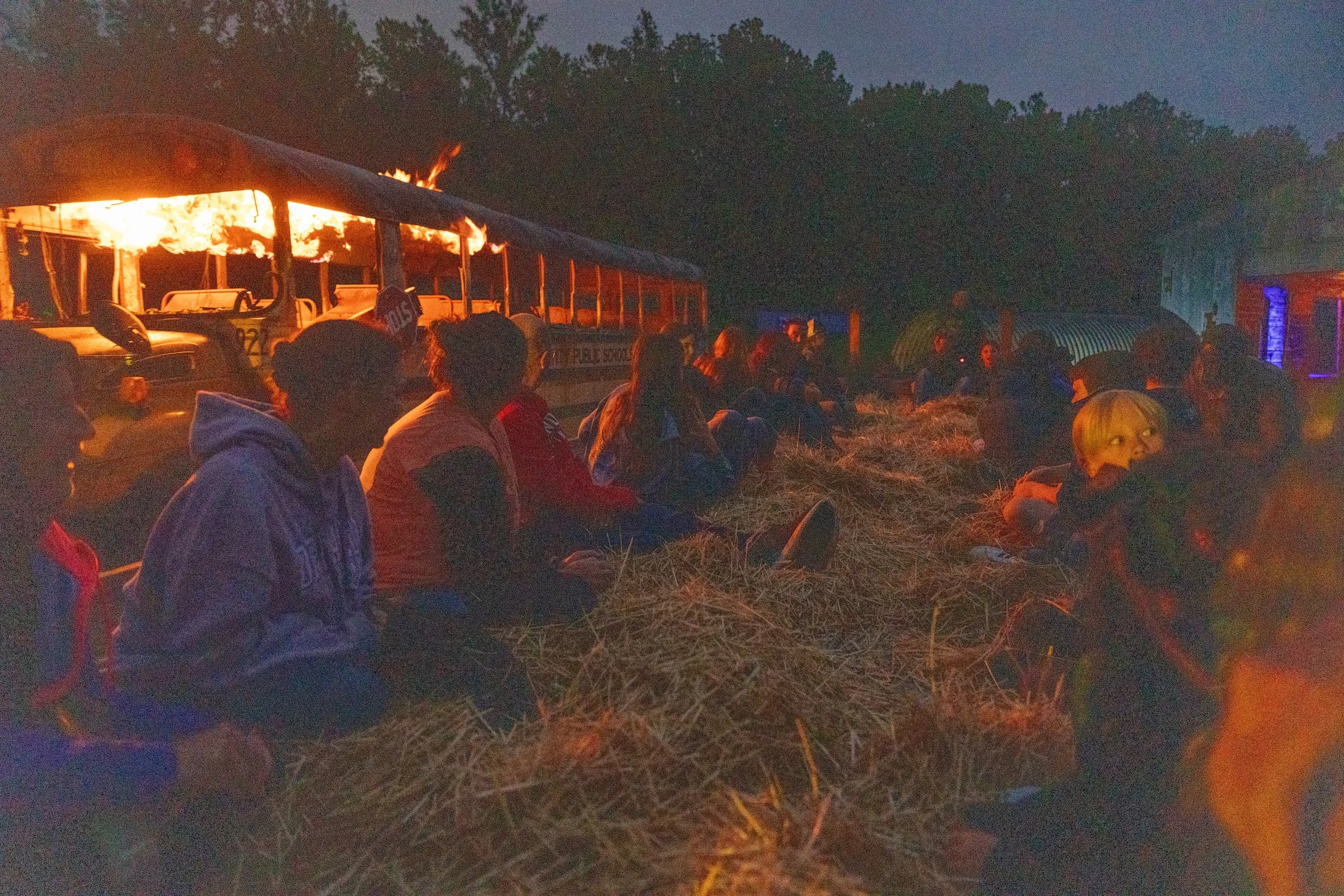 Customers riding in a hay wagon, riding by a flaming school bus.
