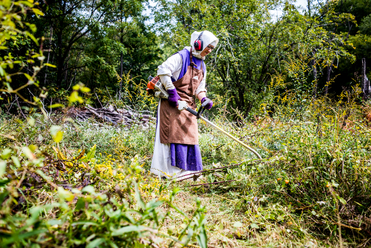  Sister Peggy using a weed trimer to clear a pasture for their cow dawn on their land. 