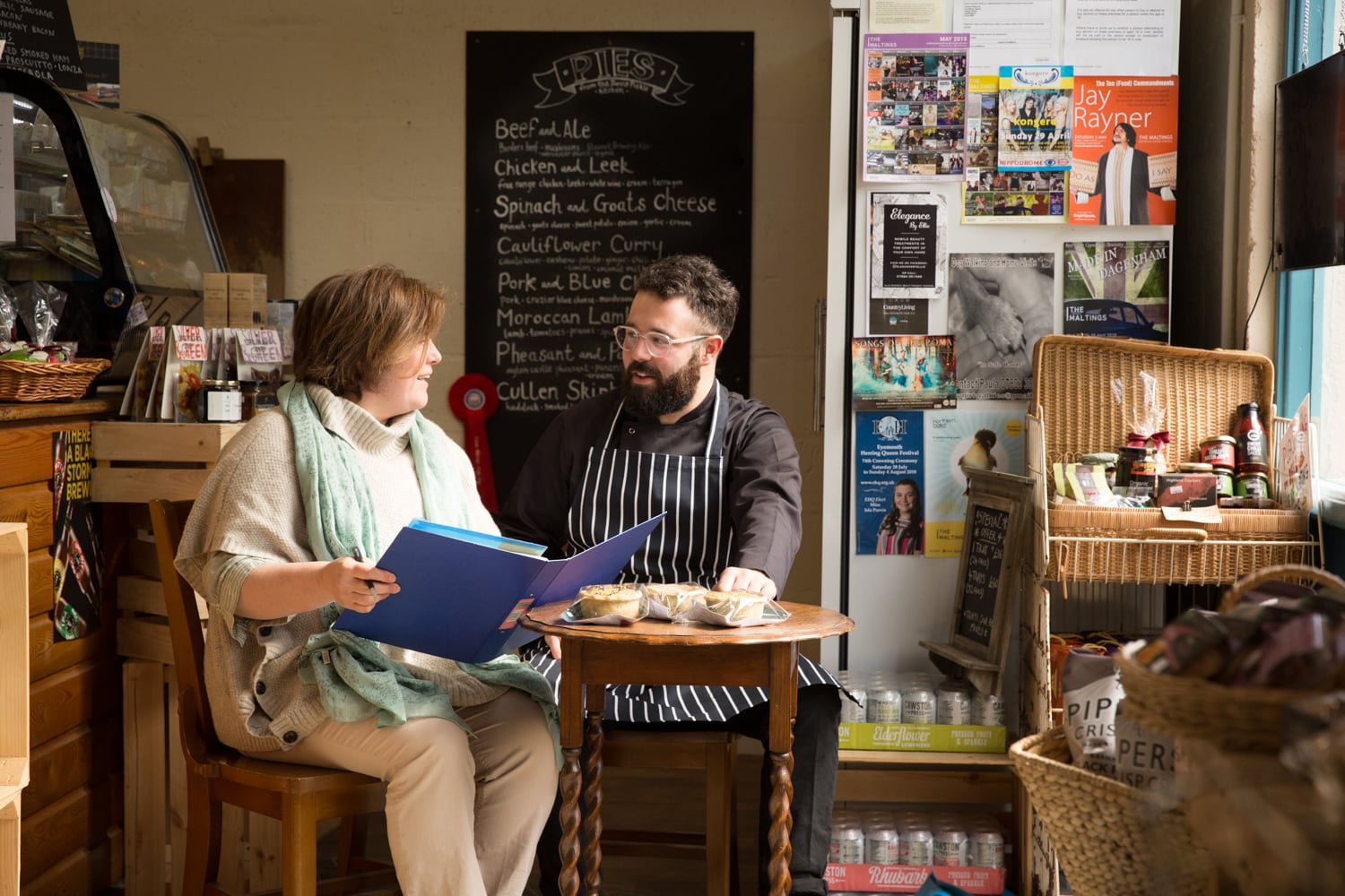 Two employees of Jarvis Pickle Pies standing at a table and acting as customers in their storefront in Eyemouth scottish borders