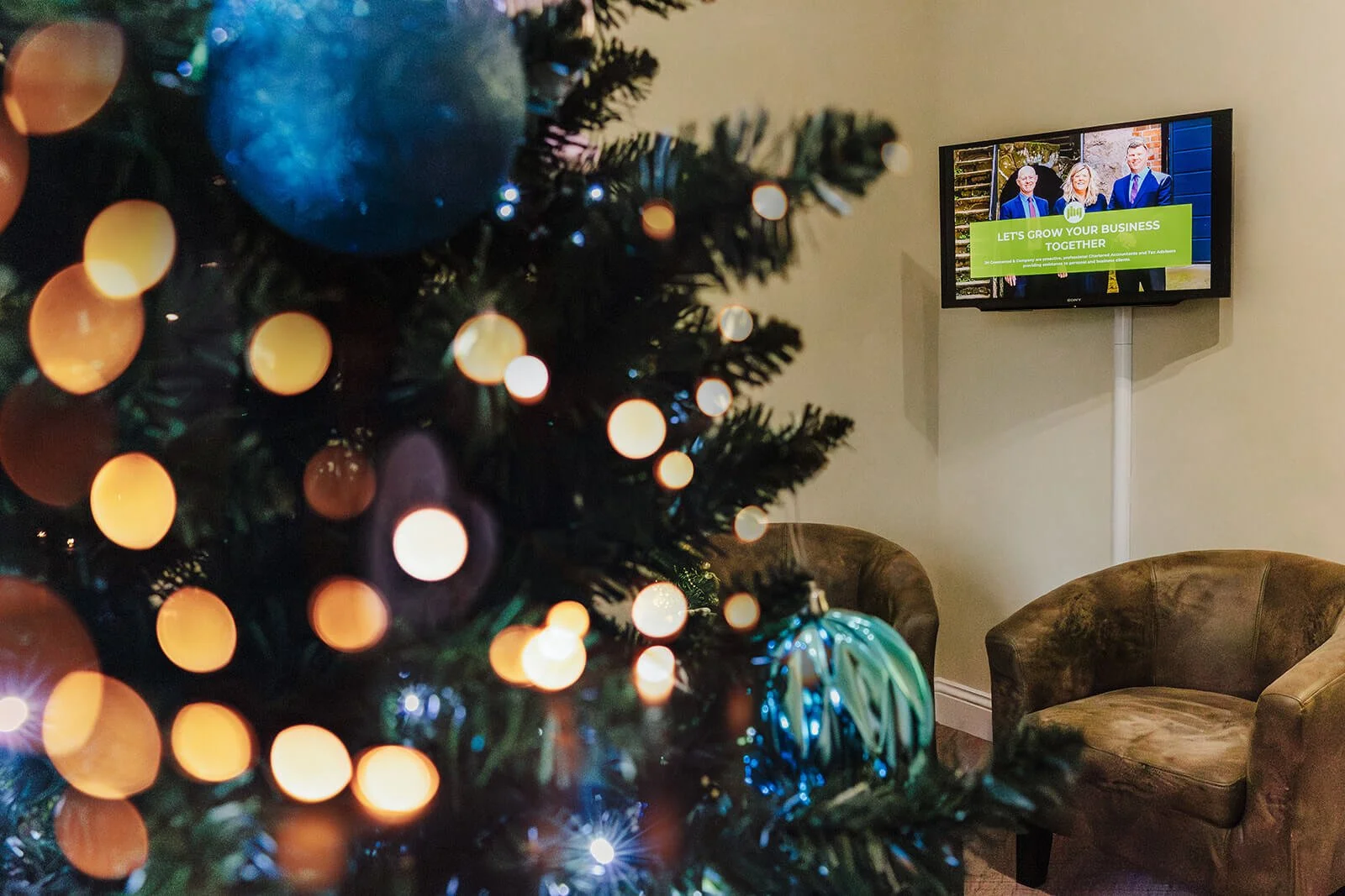 close up of christmas tree in waiting room reception area with wall mounted TV which includes brand photography of the Greenwoods team