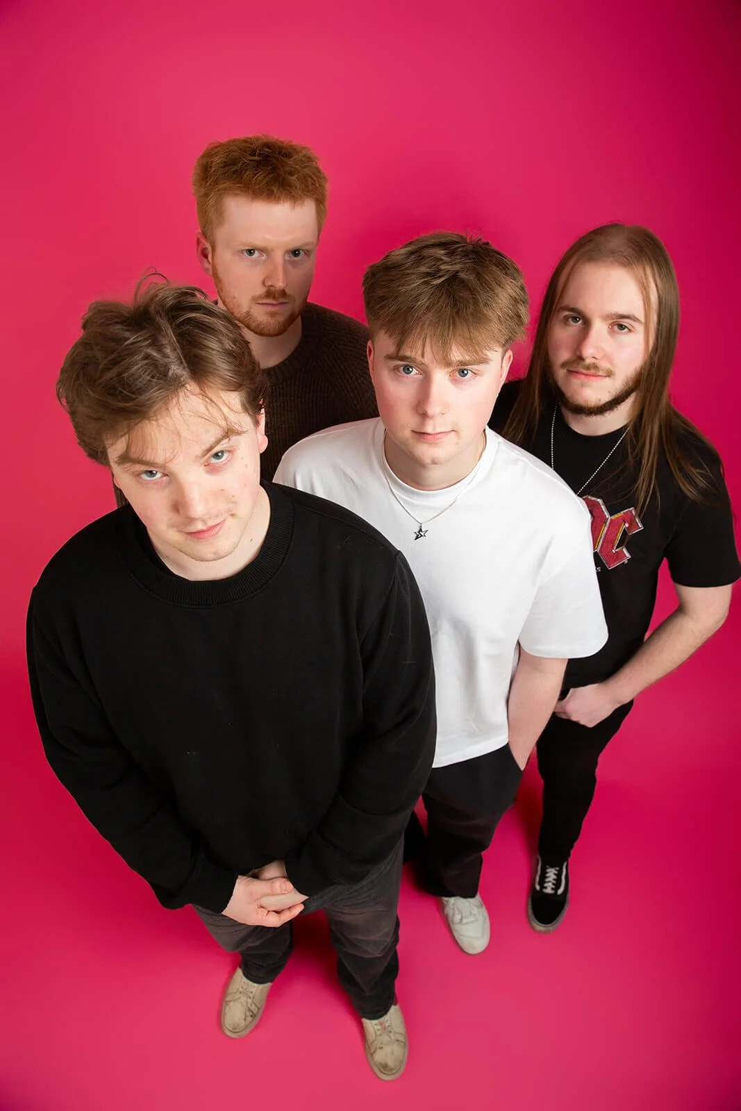 Four band members staring at camera in a studio with a pink background