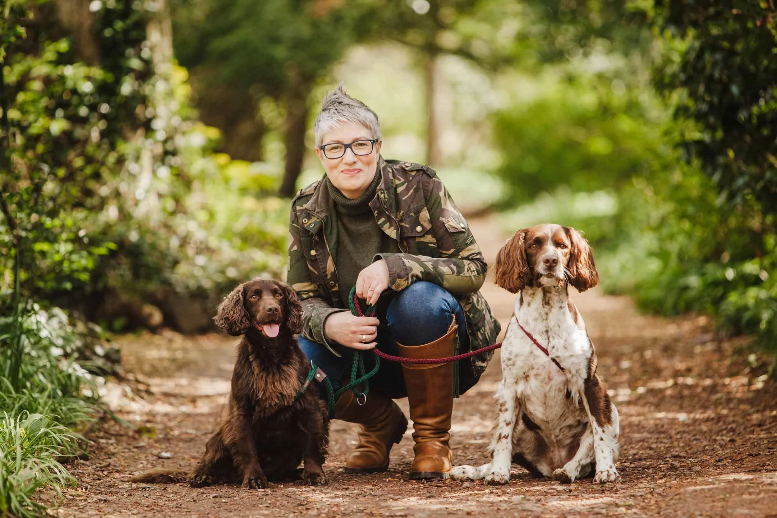 woman with short grey hair kneeling down with her two dogs on leads