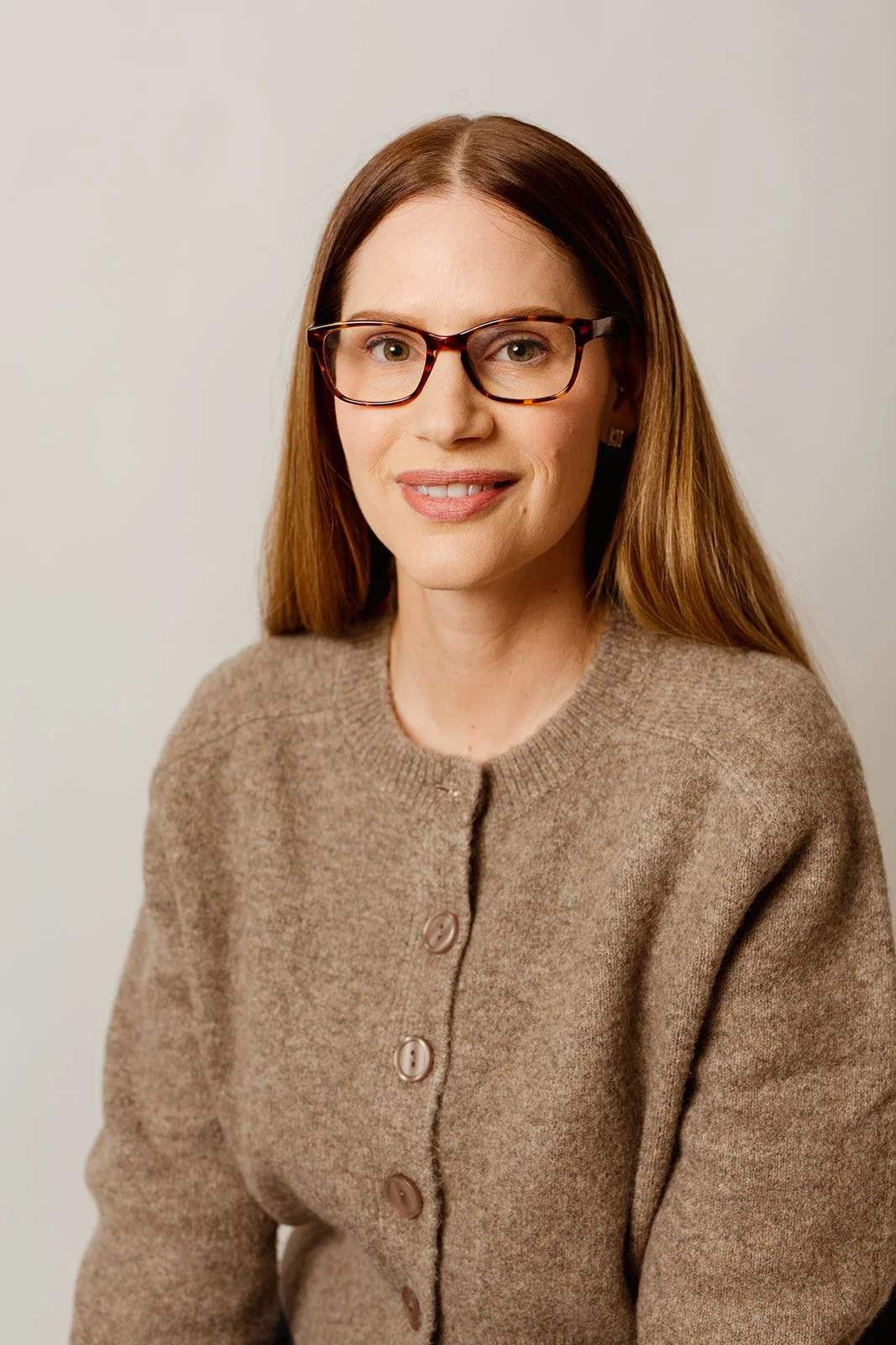 andrea wearing glasses sitting wearing brown cardigan smiling