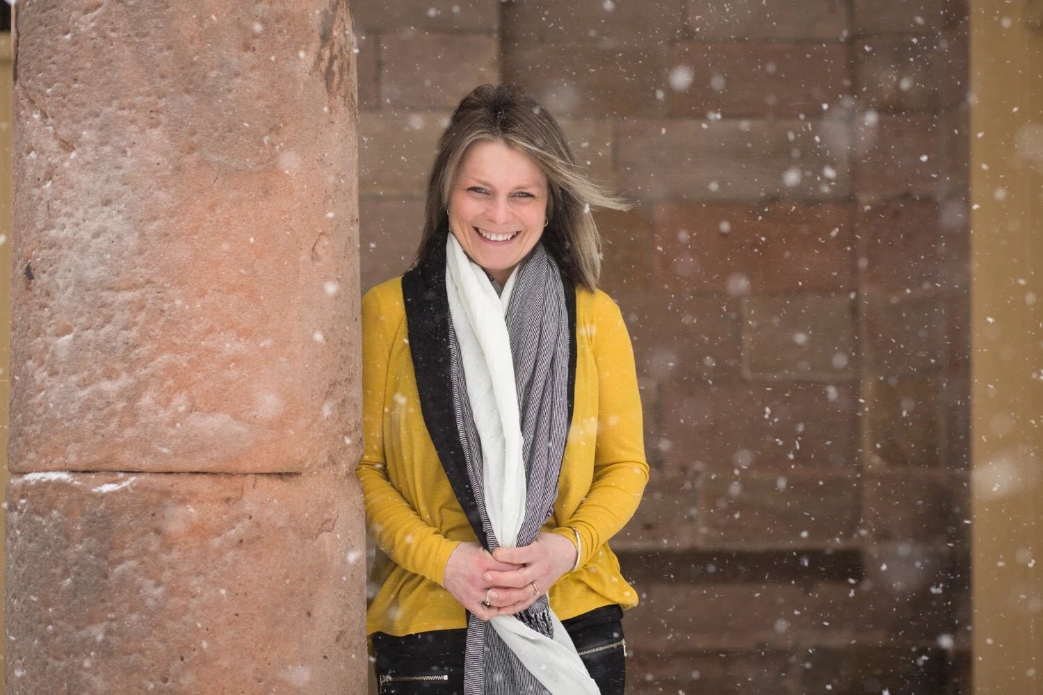 Woman smiling while leaning against a stone pillar, snow in the foreground northumberland headshots