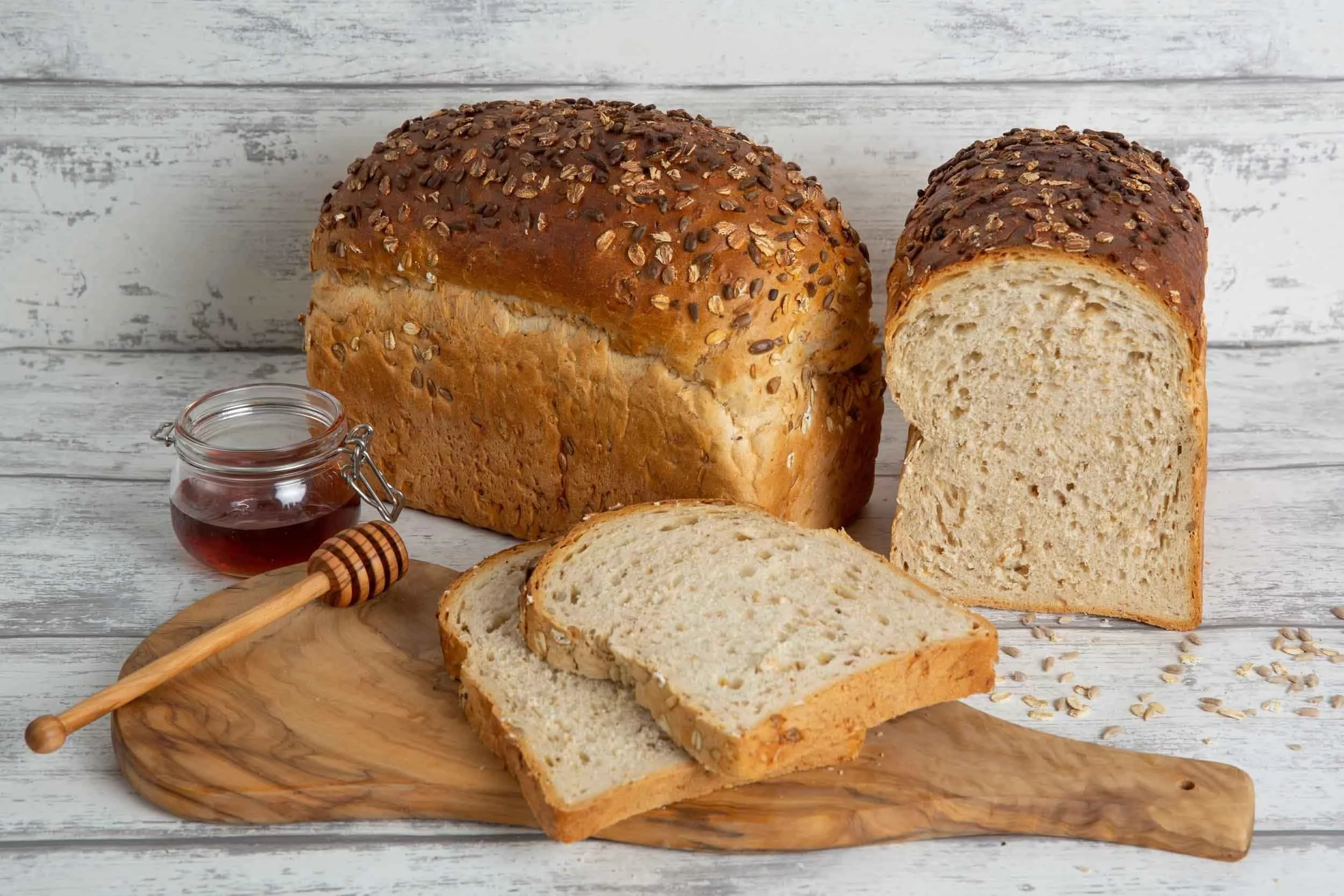 product shots of Two loaves of bread with a few slices sitting on a board with a small jar of honey next to them made in northumberland