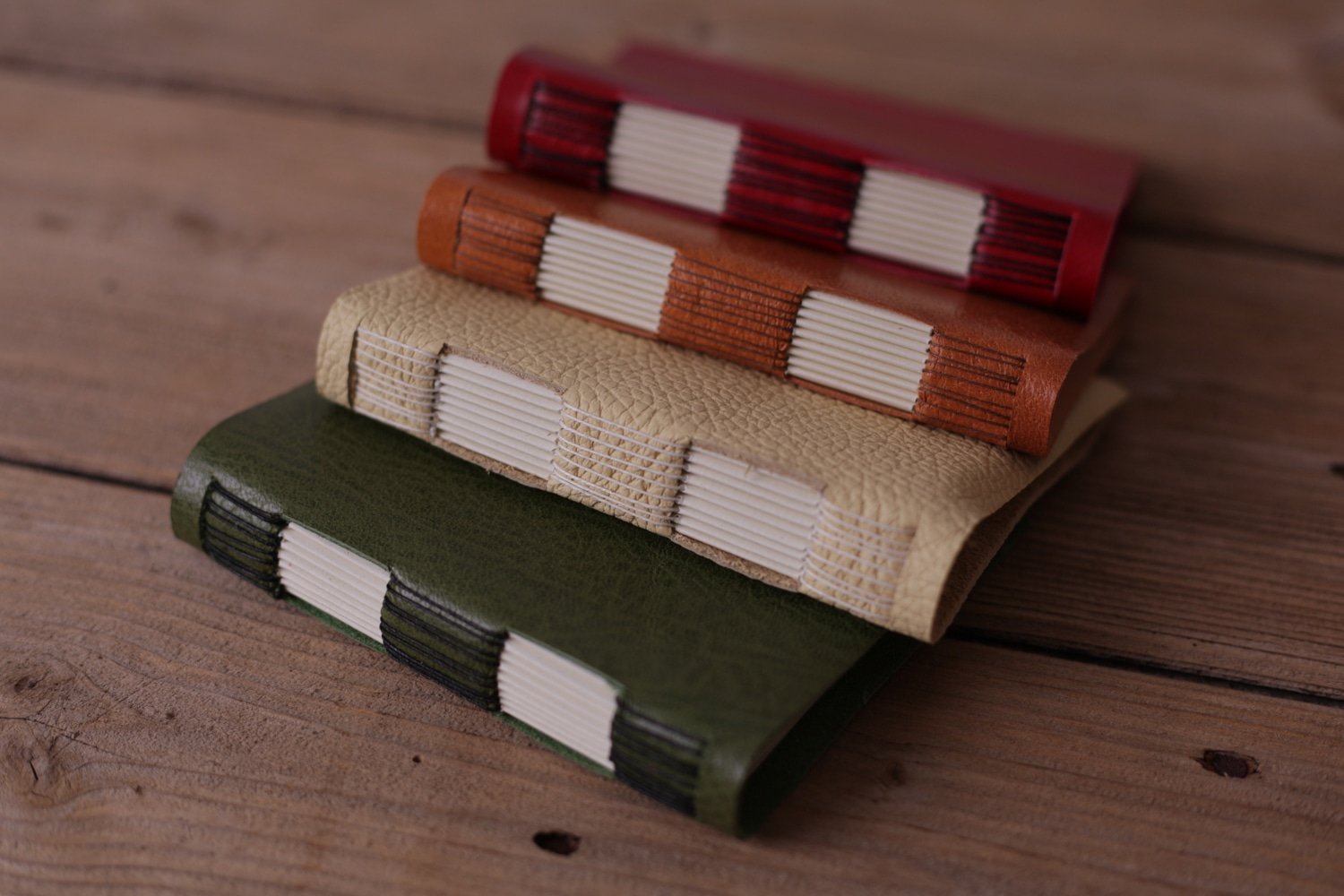 A collection of handmade leatherbound books in red, orange, cream, and green berwick craftsperson artist
