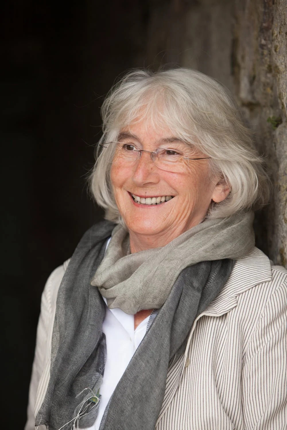 Woman with grey hair smiling away from the camera, wearing a grey scarf