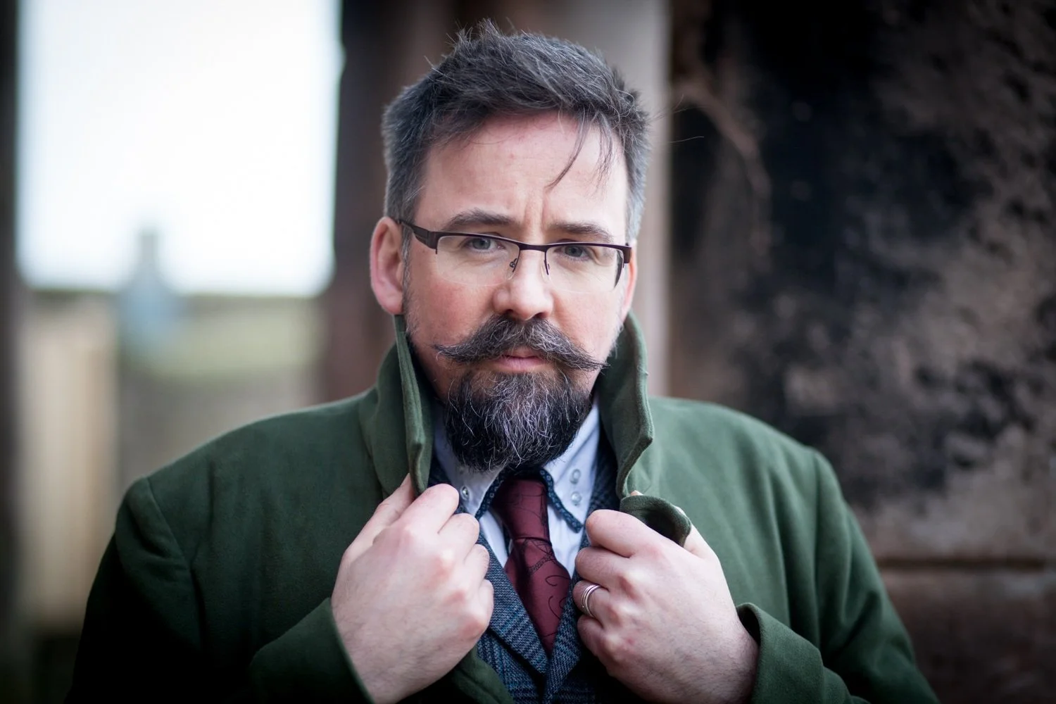 man with moustache holding lapel of jacket whilst looking into the camera lens