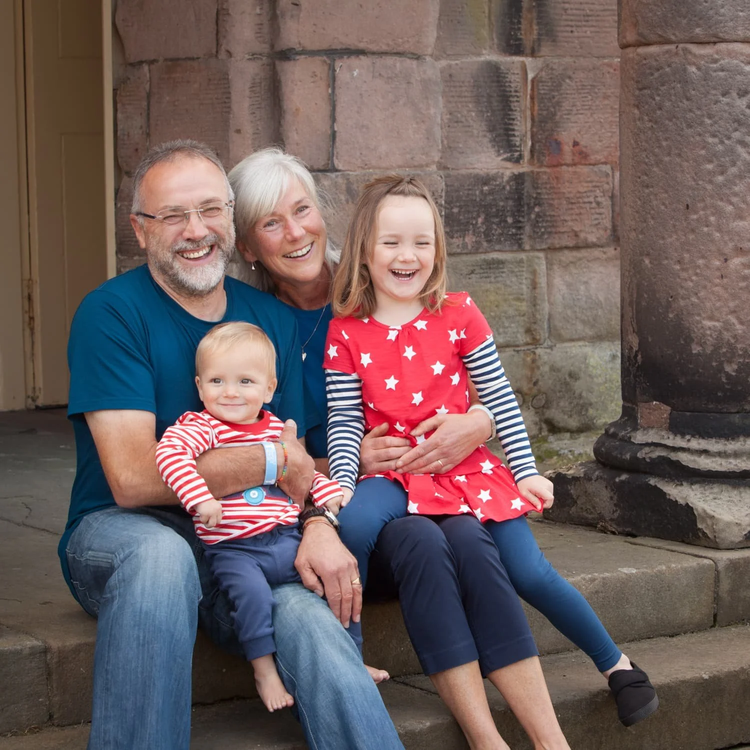 grandparents with grandchildren dressed in reds and blues sitting on old steps in historical town location