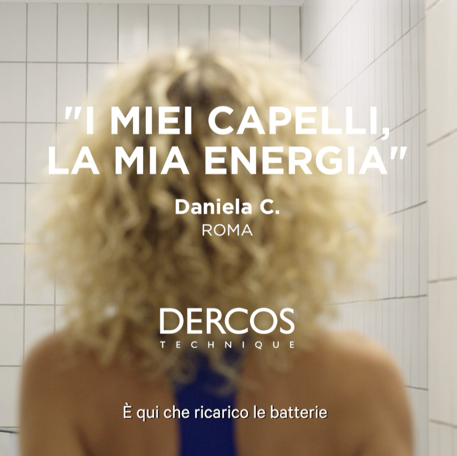 A person with curly blonde hair standing in a tiled room, facing away from the camera with text overlay in Italian and English.