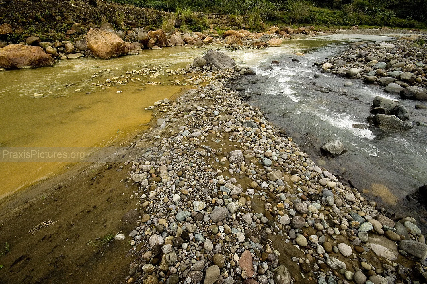 CONTAMINATED WATER - Just a few meters past the Victoria Gold Mine’s tailings dam, contaminated water (left) – carrying with it cyanide, lead, copper, and mercury – joins together with the clean water (right) coming from the mountain springs into the river system. Many mine sites are located in the mountains that act as watersheds for the surrounding river systems, which poses serious threats to those living downstream from the mines.